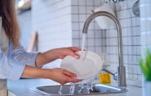 woman at kitchen sink runs water over a dish for final rinse.